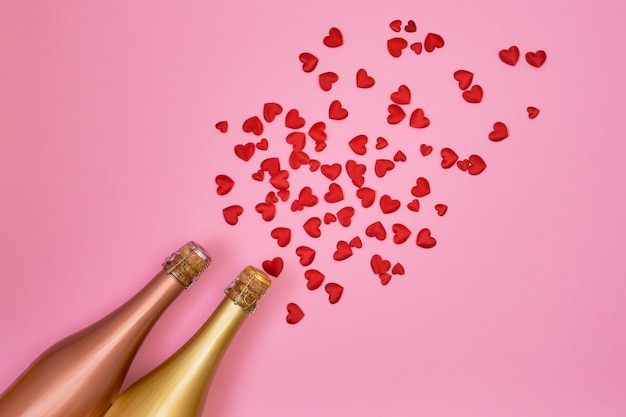 Bouteilles de champagne avec des coeurs rouges sur fond rose.