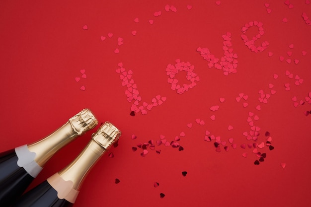 Bouteilles de champagne avec des confettis formant le mot amour sur fond rouge.