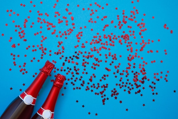 Bouteilles de champagne avec des étoiles de confettis sur bleu clair. Copier l'espace, vue de dessus