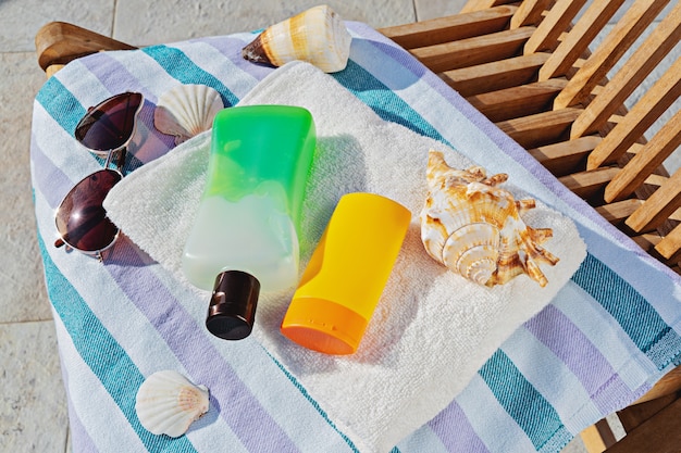 Bouteilles cosmétiques solaires et lunettes de soleil dans une serviette sur une chaise longue