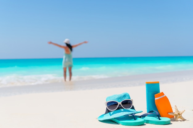 Bouteilles de crème solaire, lunettes de soleil, tongs sur le sable blanc