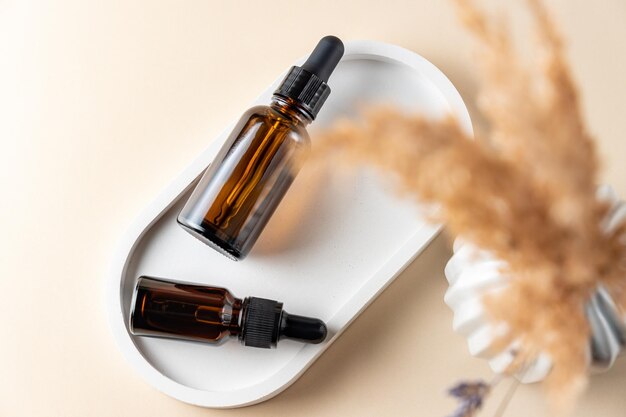 Bouteilles à gouttes en verre avec une pipette à pointe noire sur un plateau en béton et de belles fleurs Nature Concept de peau Organic Spa Cosmetics Concept à la mode