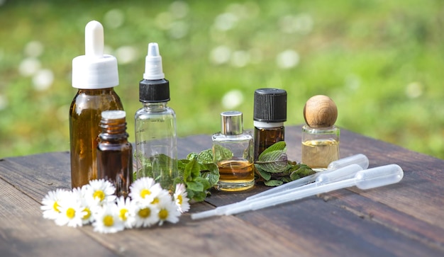 bouteilles d'huile essentielle et de marguerites avec des feuilles de menthe fraîches sur une table en bois à l'extérieur