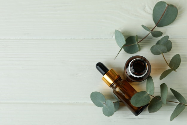 Bouteilles d'huile d'eucalyptus et brindilles sur fond de bois blanc