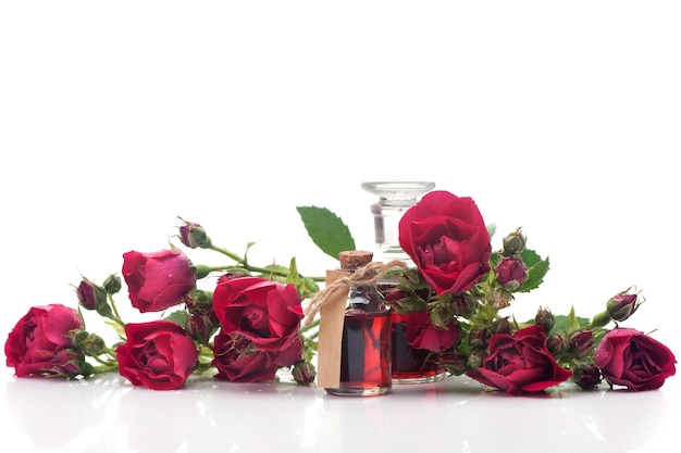 Bouteilles d'huile de rose et de fleurs roses sur fond blanc