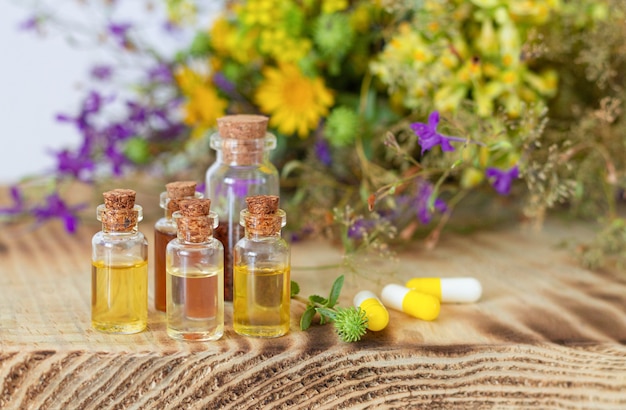 Bouteilles d'huiles essentielles naturelles à côté de pilules à base de plantes et de fleurs curatives fraîches