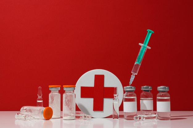 Bouteilles médicales en verre avec seringue de vaccin et boîte avec une croix rouge sur fond rouge