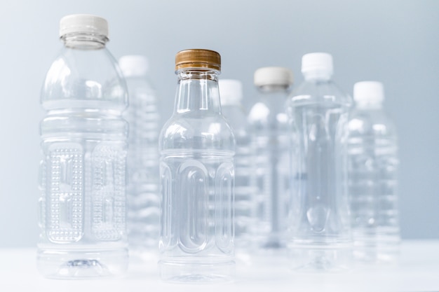 Bouteilles en plastique de différentes formes et tailles sur une table et un fond blancs