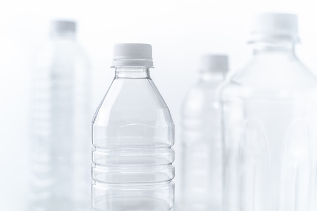 Bouteilles en plastique de différentes formes et tailles sur une table et un fond blancs