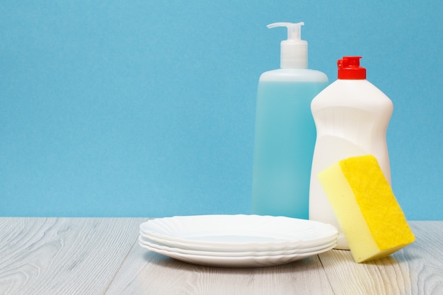 Bouteilles en plastique de liquide vaisselle, nettoyant pour vitres et carreaux, assiettes propres et éponge sur fond bleu. Concept de lavage et de nettoyage.