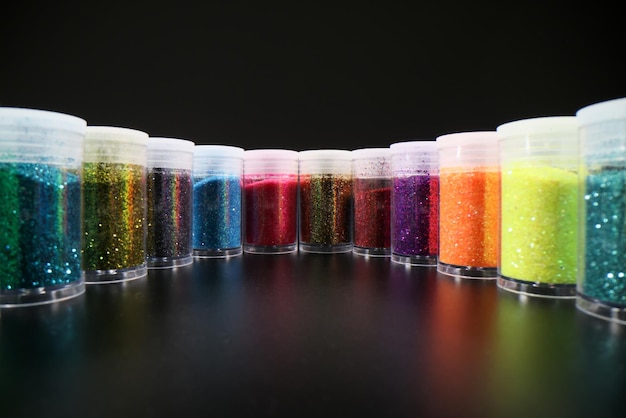 Bouteilles en plastique avec poudre de paillettes multicolores placées dans une rangée sinueuse reflétant sur une table sombre