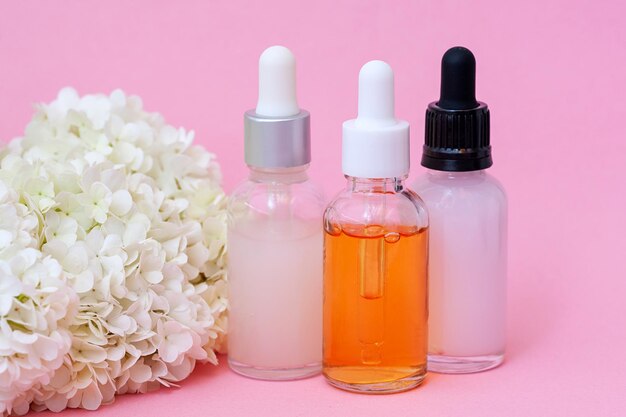 Bouteilles de sérums différents sur fond rose Concept facial