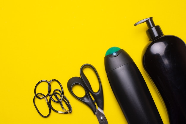 Bouteilles de shampoing noir, ciseaux et élastiques à cheveux sur une surface jaune