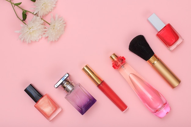 Bouteilles avec vernis à ongles, parfum, pinceau, rouge à lèvres et fleurs sur fond rose. Cosmétiques et accessoires pour femmes. Vue de dessus.