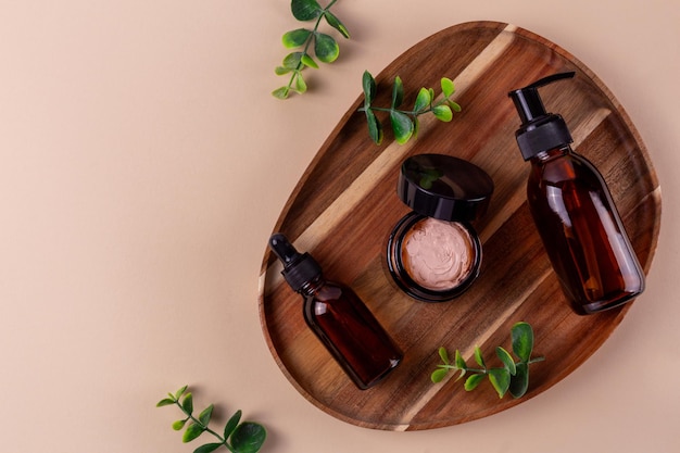 Photo bouteilles de verre cosmétiques en ambre foncé et accessoires de bain sur support en bois sur fond beige produits de beauté de salle de bain respectueux de l'environnementxa