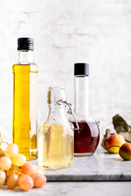 Bouteilles en verre d'origine avec du vinaigre différent sur une table en marbre contre une table d'un mur de briques blanches. Copiez l'espace. Verticale.