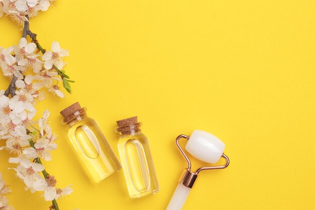 Bouteilles en verre avec rouleau à huile pour le massage du visage sur fond jaune avec cerisier en fleurs Soins cosmétiques de la peau du visage et spa Concept de traitement naturel