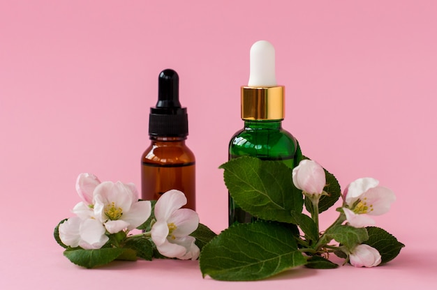 Bouteilles en verre de sérum avec pipette et belle fleur sur fond rose. Concept cosmétique de Spa bio naturel. Vue de face.