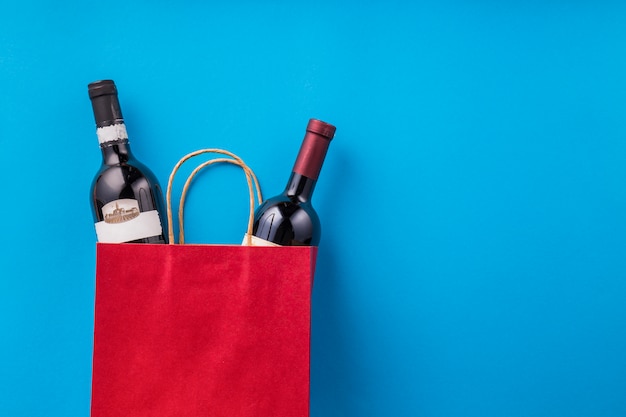 Bouteilles de vin dans un sac shopping rouge contre le papier peint bleu