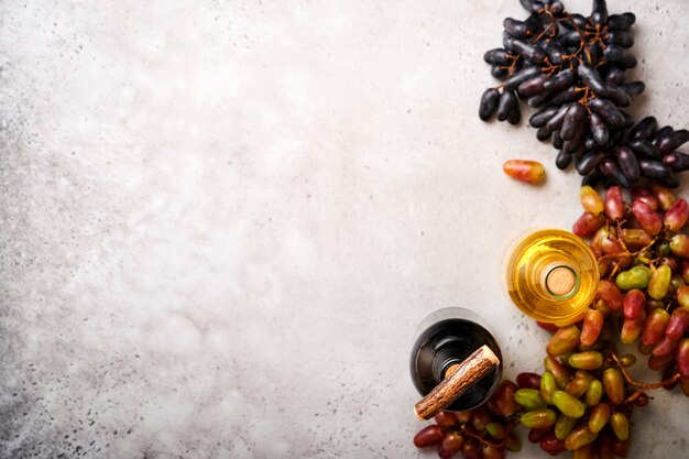 Bouteilles de vin avec raisins et verres à vin sur fond de table en béton gris ancien avec espace de copie. Vin rouge avec une branche de vigne. Composition de vin sur fond rustique. Maquette.