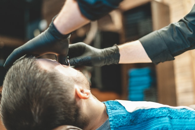 Boutique de beauté pour hommes. Se raser la barbe dans un salon de coiffure. Barber coupe sa barbe avec un rasoir et une tondeuse. bouchent les coupes de cheveux brutales. Matériel de coiffeur. Mise au point sélective.