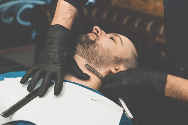 Boutique de beauté pour hommes. Se raser la barbe dans un salon de coiffure. Barber coupe sa barbe avec un rasoir et une tondeuse. bouchent les coupes de cheveux brutales. Matériel de coiffeur. Mise au point sélective.