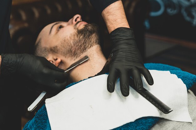 Boutique de beauté pour hommes. Se raser la barbe dans un salon de coiffure. Barber coupe sa barbe avec un rasoir et une tondeuse. bouchent les coupes de cheveux brutales. Matériel de coiffeur. Mise au point sélective.