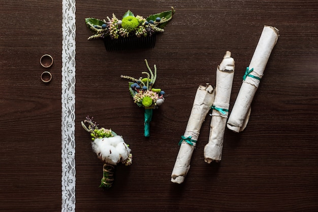 Boutonnière en coton posée sur une table marron avec dentelle, rouleaux de parchemin ancien