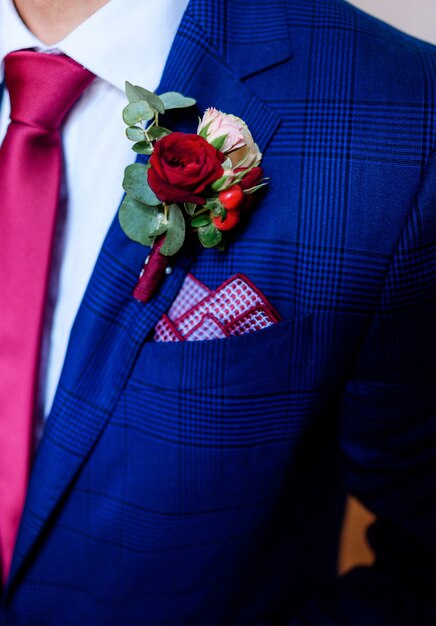 Boutonnière rouge foncé épinglée à la veste bleue du marié