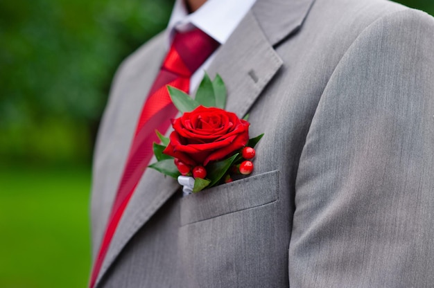 Boutonnière rouge sur la veste du marié gris