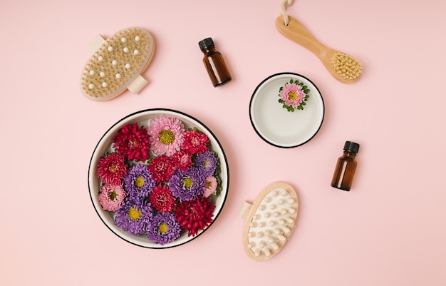 Photo boutons de fleurs de chrysanthème rose et violet flottant dans des bols ronds blancs avec de l'eau et des accessoires cosmétiques de beauté sur fond rose. mise à plat naturelle minimale. produits de bien-être écologiques.