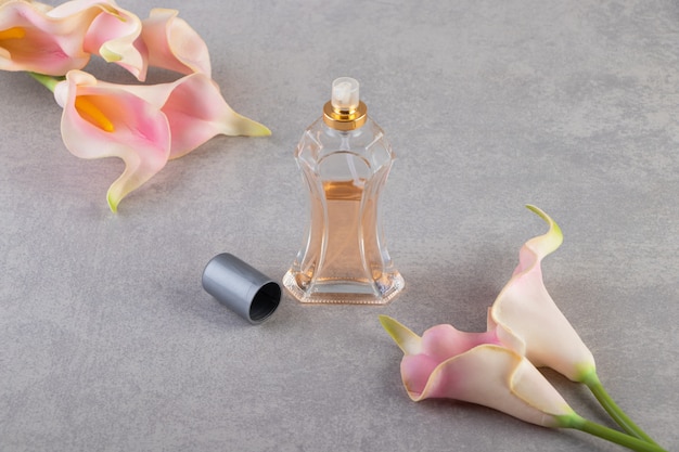 Boutons de fleurs roses artificielles avec bouteille de parfum sur pierre.