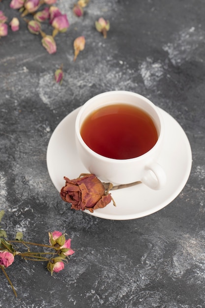 Boutons de rose séchés avec une tasse de thé chaud posé sur une table en pierre.