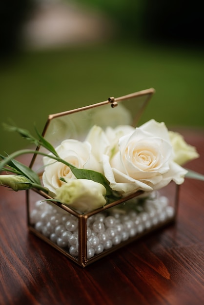 Boutons de roses blancs dans une boîte en verre pour alliances