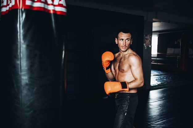 Photo boxer masculin formation avec sac de boxe dans une salle de sport sombre.