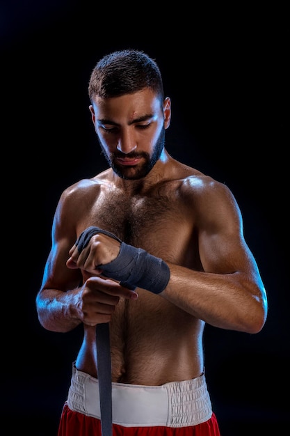 Boxer préparant ses gants pour un combat. Photo d'un homme musclé attachant les mains sur fond noir.