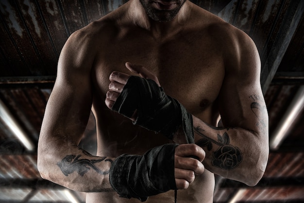 Boxer avec des tatouages et des muscles met les bandes à ses mains