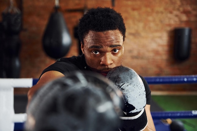 Un boxeur afro-américain fort en vêtements sportifs s'entraîne dans la salle de sport