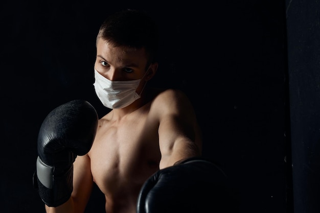 Boxeur avec un masque médical et des gants de boxe sur un fond noir Photo de haute qualité
