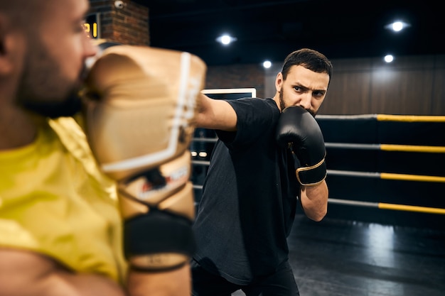 Boxeur prudent en tenue de sport noire frappant son partenaire d'entraînement d'un coup droit à la tête