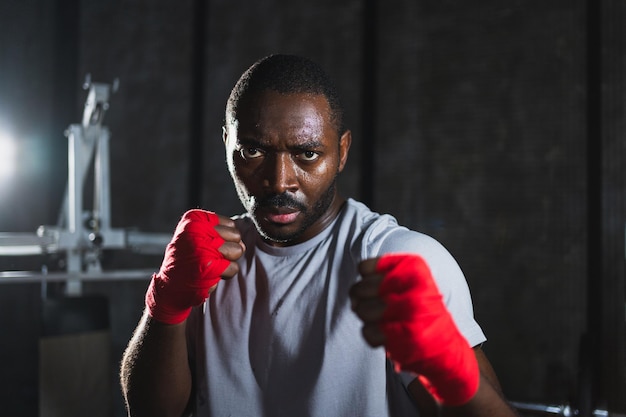 Boxeur en salle de sport homme africain agressif combattant se reposant après l'entraînement de boxe prêt pour le combat en regardant