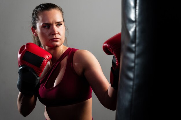 Photo une boxeuse en combinaison rouge frappe un sac de boxe sur un fond sombre