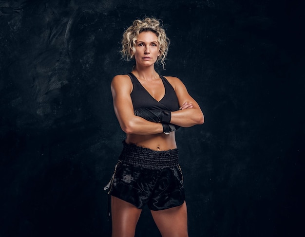 Une boxeuse expérimentée pose pour un photographe dans un studio photo sombre avec les mains croisées.