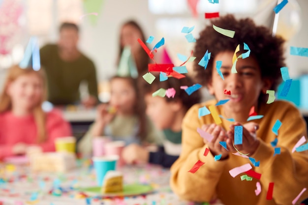 Photo boy blowing confetti at camera à l'anniversaire avec des amis et des parents à la maison