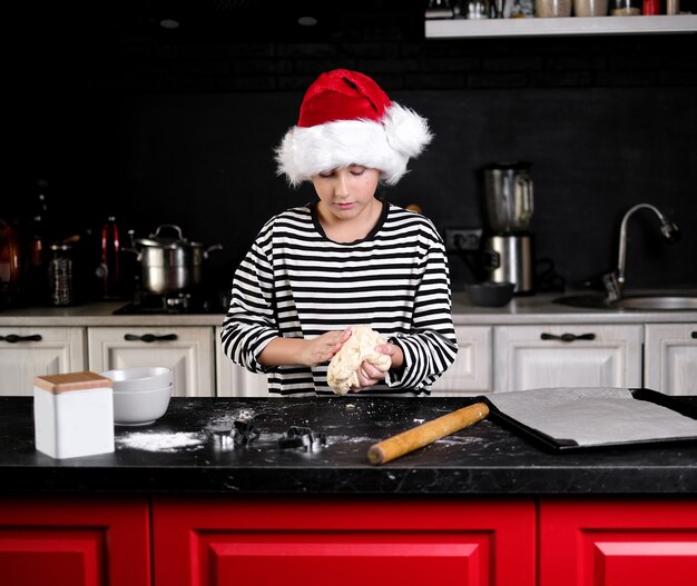 Boy in Santas hat fait des pâtisseries pour Noël à la cuisine