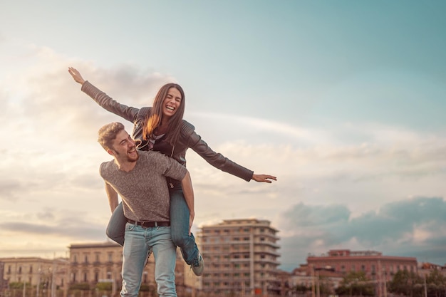 Boyfriend piggybacking petite amie dans la ville contre le ciel