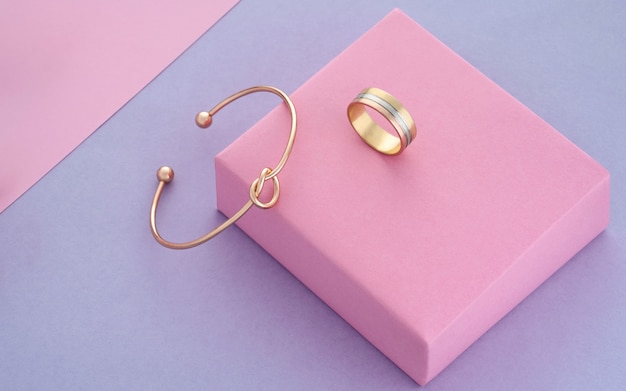 Bracelet et bague dorés en forme de noeud sur fond de papier rose et violet avec espace de copie