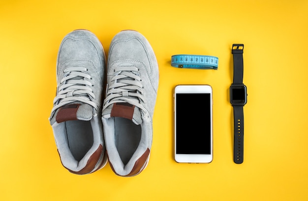 Bracelet de remise en forme, baskets, téléphone portable et ruban adhésif sur fond jaune. Séance d'entraînement à plat