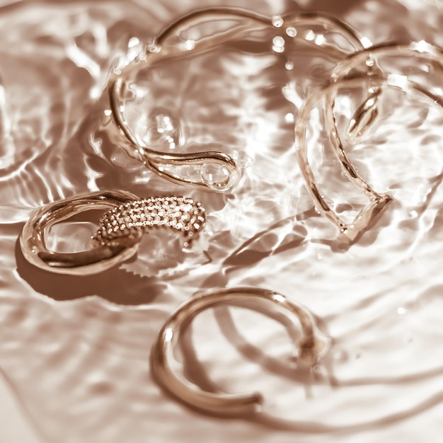 Bracelets dorés boucles d'oreilles bagues bijoux sur fond d'eau dorée glamour de luxe et conception de beauté de vacances pour les annonces de marque de bijoux