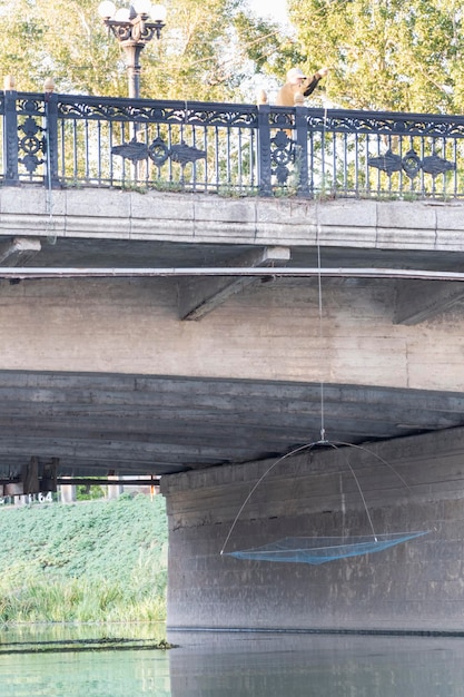 Un braconnier debout sur un pont de la ville pêche un filet dans la rivière